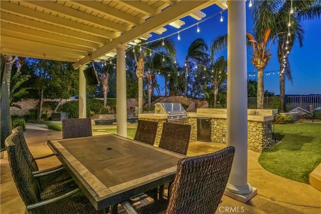 patio at twilight featuring a pergola, a grill, and exterior kitchen