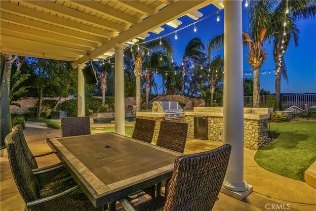 patio at twilight featuring a fenced backyard, a lawn, area for grilling, outdoor dining space, and an outdoor kitchen