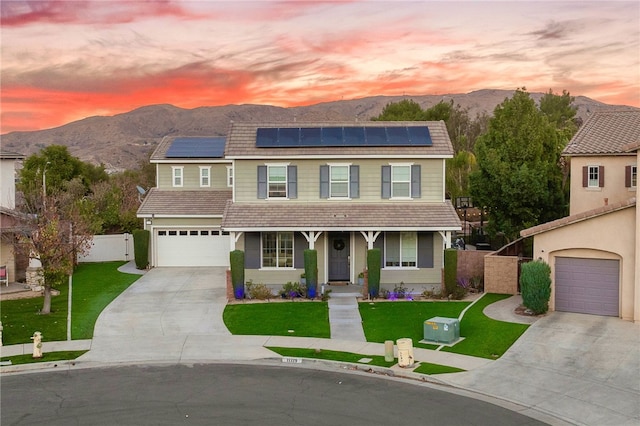 view of front of house featuring a porch, a lawn, solar panels, a garage, and a mountain view