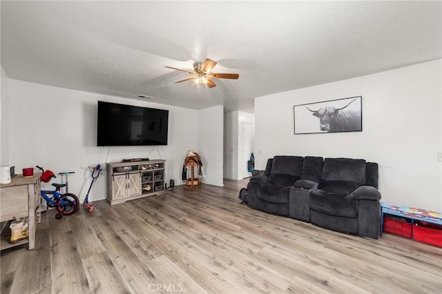 living room featuring a textured ceiling, light wood-type flooring, and ceiling fan