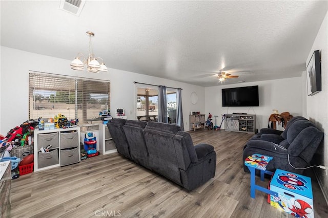 living room with ceiling fan with notable chandelier, light wood-type flooring, and a textured ceiling