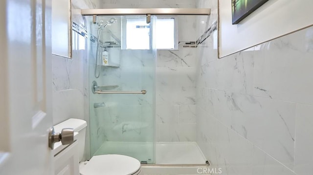 bathroom featuring a shower with door and toilet