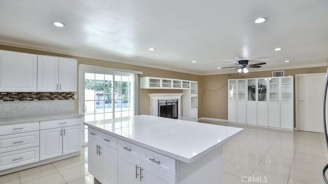 kitchen featuring backsplash, ceiling fan, light tile patterned floors, a kitchen island, and white cabinetry