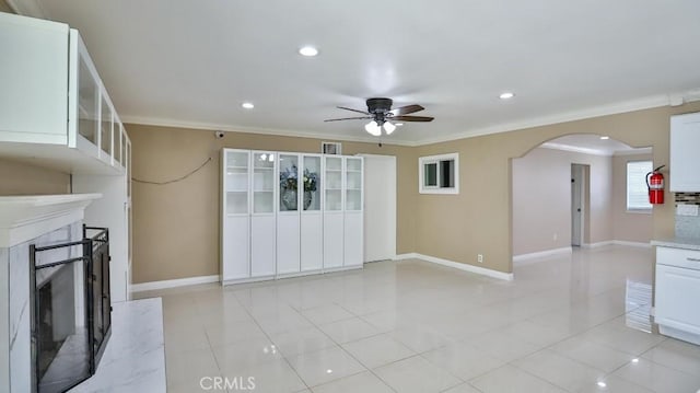 unfurnished living room with light tile patterned floors, ceiling fan, crown molding, and a premium fireplace