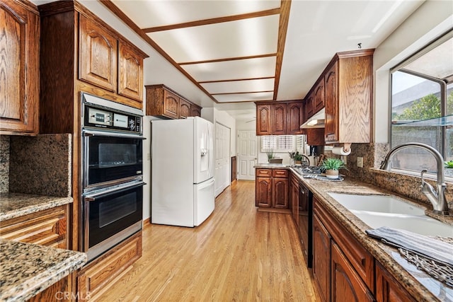 kitchen featuring light stone countertops, light hardwood / wood-style floors, tasteful backsplash, and black appliances