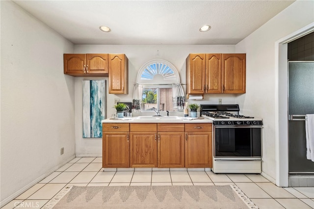 kitchen featuring black refrigerator, sink, light tile patterned floors, and range with gas stovetop