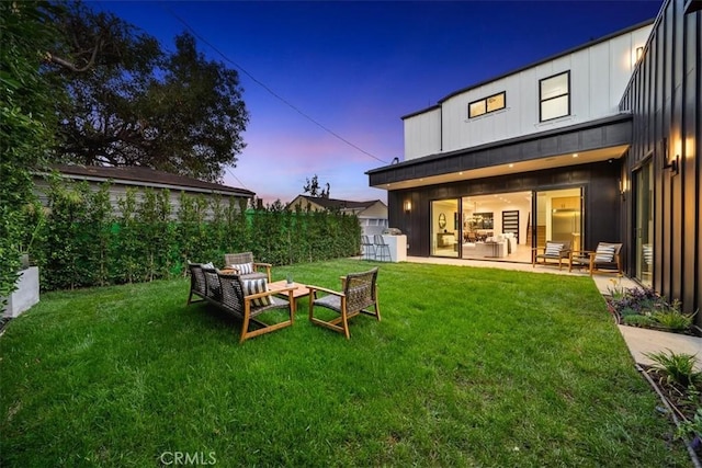 back house at dusk featuring a yard, an outdoor hangout area, and a patio