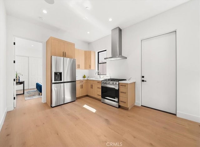 kitchen featuring appliances with stainless steel finishes, light wood-type flooring, light brown cabinetry, and wall chimney range hood