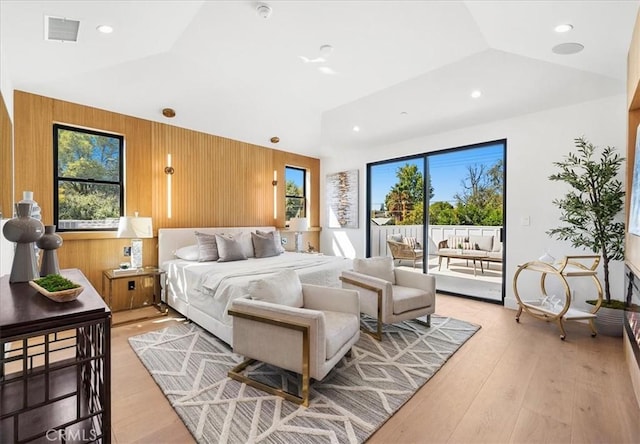 bedroom with wood walls, light hardwood / wood-style floors, access to outside, and vaulted ceiling