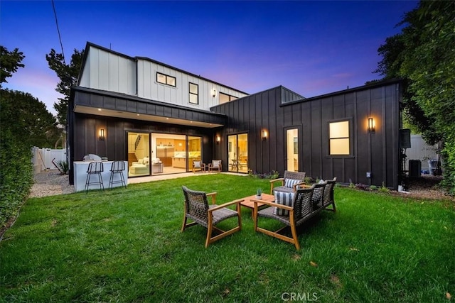 back house at dusk with an outdoor hangout area, a patio, and a lawn