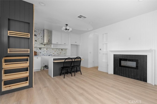 kitchen with a kitchen bar, wall chimney exhaust hood, a center island, white cabinetry, and a tiled fireplace