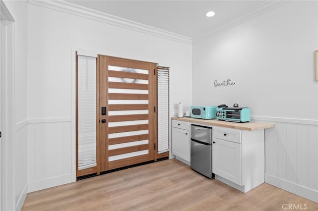 kitchen featuring wooden counters, white cabinets, light wood-type flooring, ornamental molding, and stainless steel refrigerator