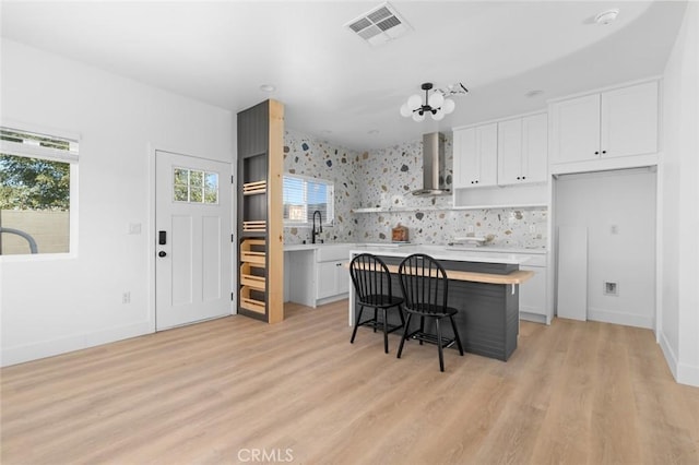 kitchen featuring white cabinets, a center island, wall chimney range hood, and a breakfast bar area