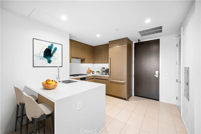 kitchen featuring sink, gas stovetop, light tile patterned floors, kitchen peninsula, and a breakfast bar area