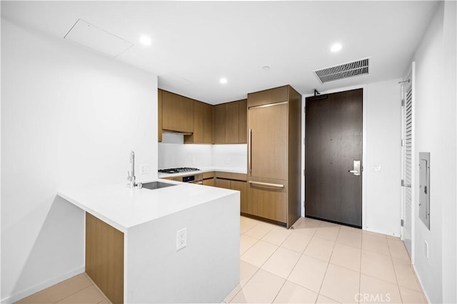 kitchen with kitchen peninsula, sink, light tile patterned flooring, and stainless steel gas cooktop