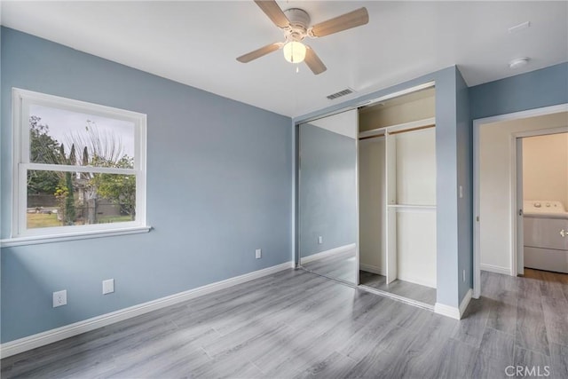 unfurnished bedroom featuring washer / clothes dryer, ceiling fan, light wood-type flooring, and a closet