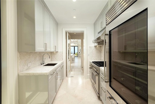 kitchen featuring sink, high end stainless steel range, tasteful backsplash, light tile patterned flooring, and light stone counters