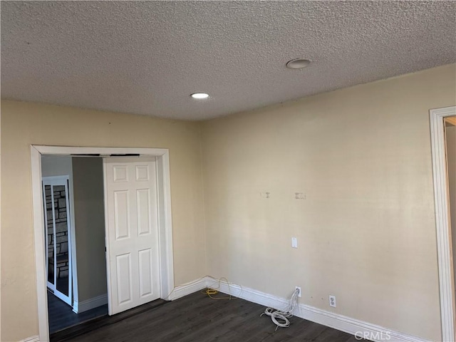 unfurnished room with dark wood-type flooring, a textured ceiling, and baseboards