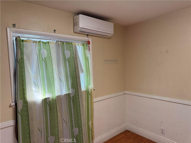 spare room featuring baseboards, an AC wall unit, and wood finished floors