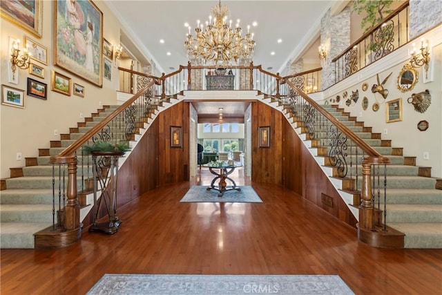 foyer entrance featuring hardwood / wood-style flooring, crown molding, a towering ceiling, and a notable chandelier