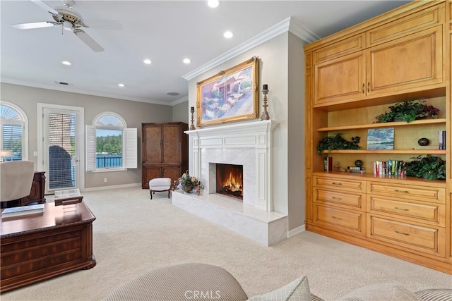 living room with a high end fireplace, light colored carpet, ceiling fan, and crown molding