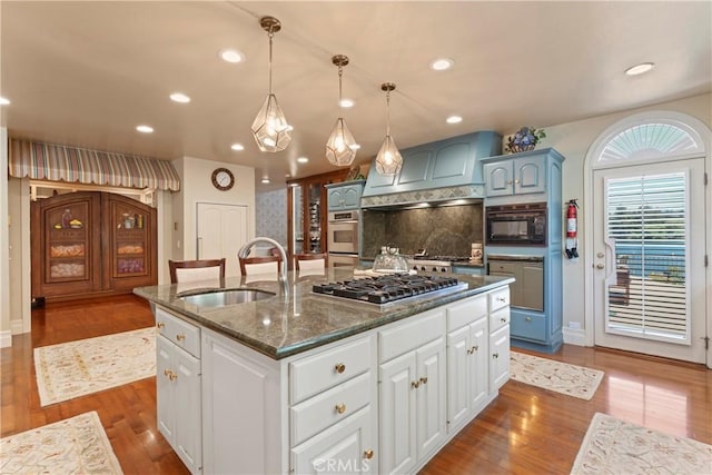 kitchen featuring appliances with stainless steel finishes, tasteful backsplash, sink, decorative light fixtures, and an island with sink