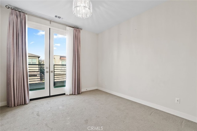 carpeted spare room featuring french doors and an inviting chandelier