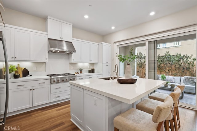 kitchen with a kitchen island with sink, sink, hardwood / wood-style flooring, white cabinetry, and stainless steel gas stovetop