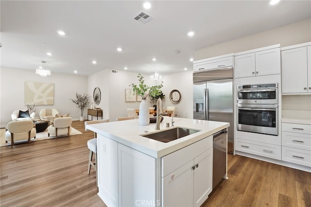 kitchen with hardwood / wood-style floors, a kitchen island with sink, sink, white cabinetry, and stainless steel appliances