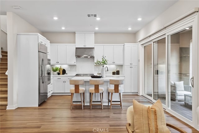 kitchen with a kitchen island with sink, white cabinets, sink, light wood-type flooring, and a breakfast bar area