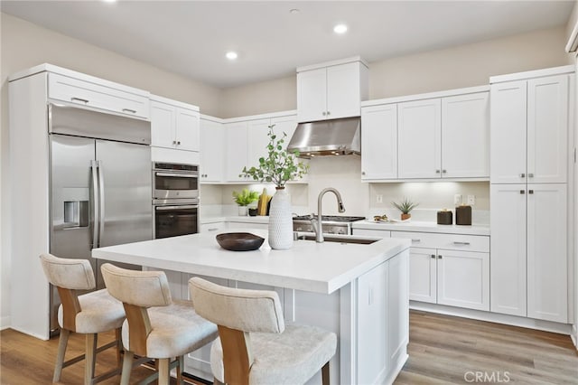 kitchen featuring appliances with stainless steel finishes, a breakfast bar, a center island with sink, light hardwood / wood-style flooring, and white cabinetry