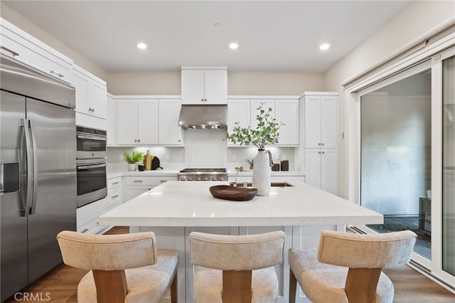 kitchen with white cabinets, stainless steel appliances, dark wood-type flooring, and an island with sink