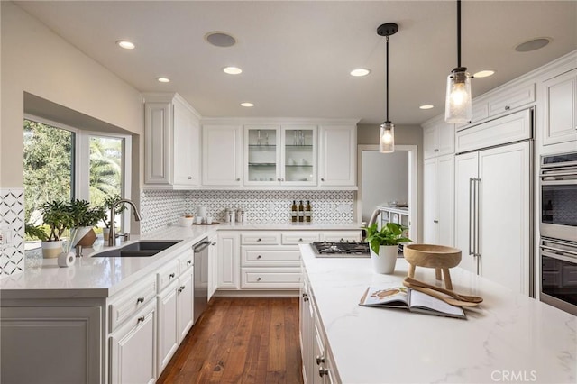 kitchen featuring pendant lighting, appliances with stainless steel finishes, sink, white cabinetry, and light stone countertops