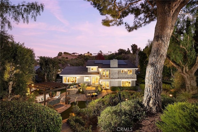 back house at dusk featuring a balcony, a patio, a pergola, and solar panels