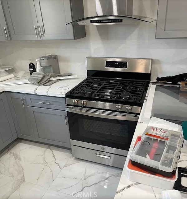 kitchen with gray cabinets, gas range, light stone counters, and wall chimney exhaust hood