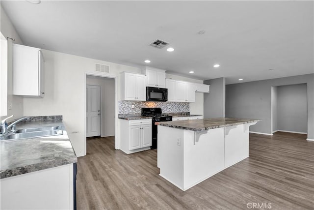 kitchen with sink, white cabinetry, a kitchen bar, a kitchen island, and black appliances