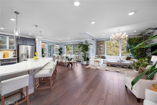 interior space with appliances with stainless steel finishes, hanging light fixtures, ornamental molding, dark wood-type flooring, and a breakfast bar area