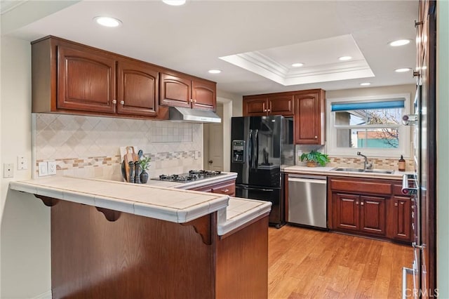 kitchen featuring tile counters, stainless steel appliances, sink, kitchen peninsula, and a raised ceiling