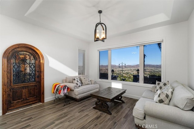 living room with a mountain view, dark wood-type flooring, a raised ceiling, and a chandelier