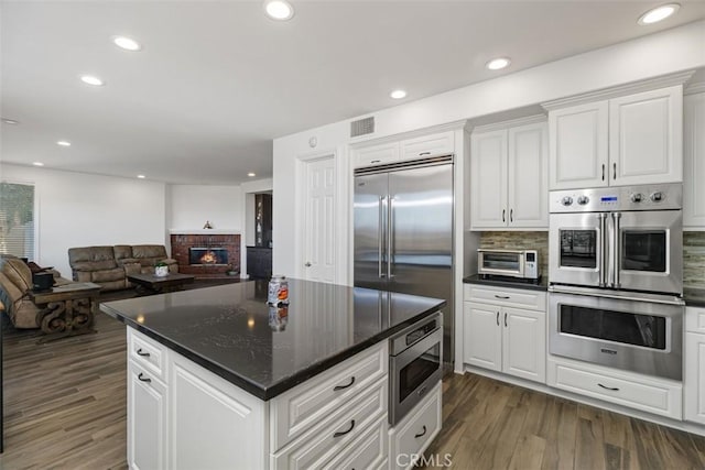 kitchen with white cabinets, a brick fireplace, built in appliances, and backsplash