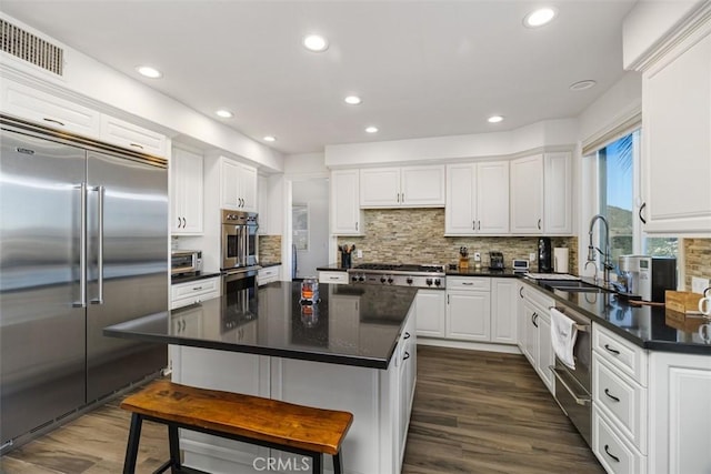 kitchen with stainless steel appliances, a kitchen island, white cabinets, backsplash, and sink