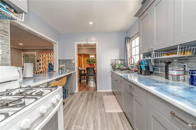 kitchen featuring sink, tasteful backsplash, gray cabinets, light hardwood / wood-style floors, and white gas range oven