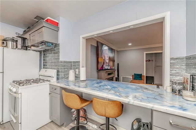 kitchen featuring gas range gas stove, a breakfast bar, gray cabinetry, tasteful backsplash, and built in desk