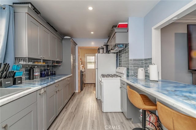 kitchen with gray cabinets, decorative backsplash, white gas range oven, light stone countertops, and light hardwood / wood-style flooring