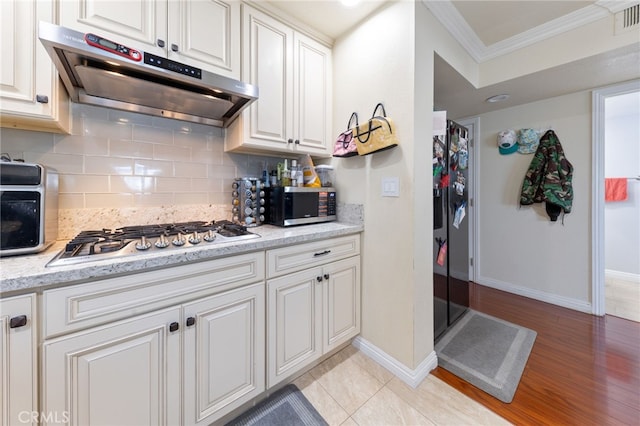 kitchen featuring white cabinetry, stainless steel appliances, tasteful backsplash, ornamental molding, and light stone counters