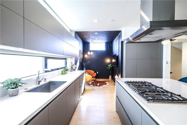 kitchen featuring stainless steel gas stovetop, island range hood, gray cabinetry, light hardwood / wood-style flooring, and sink