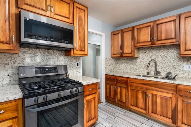 kitchen featuring light stone counters, a sink, appliances with stainless steel finishes, brown cabinets, and tasteful backsplash