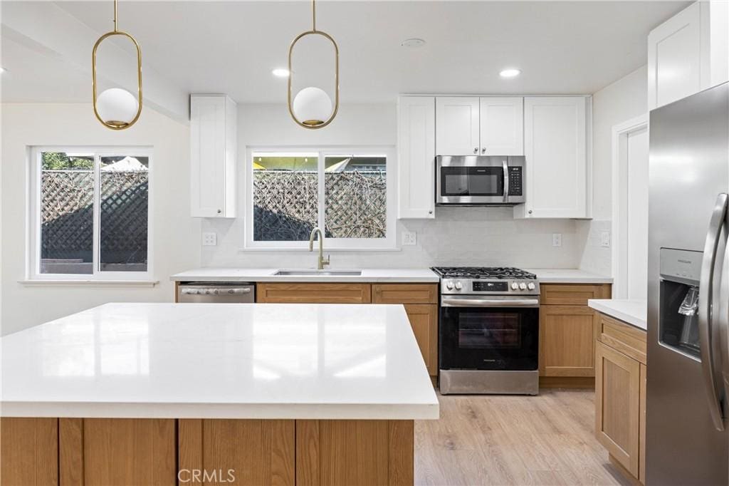 kitchen featuring stainless steel appliances, white cabinetry, sink, and decorative light fixtures