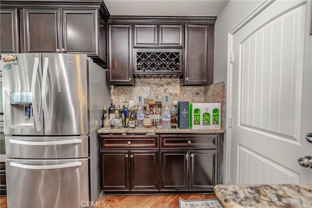 bar featuring light hardwood / wood-style floors, light stone countertops, decorative backsplash, stainless steel refrigerator with ice dispenser, and dark brown cabinetry