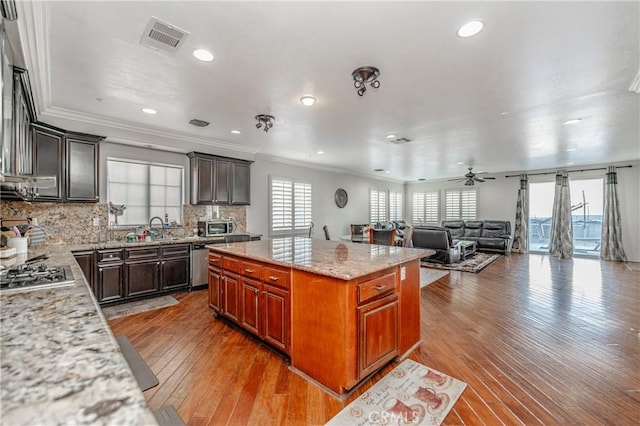 kitchen featuring light stone counters, a center island, light wood-type flooring, appliances with stainless steel finishes, and ceiling fan